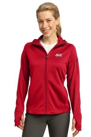 A person smiling while wearing a red, long-sleeved, full-zip hooded athletic jacket with thumb holes and a white logo.