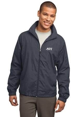 A smiling person wearing a dark blue zip-up windbreaker with a white logo on the chest, paired with gray trousers.