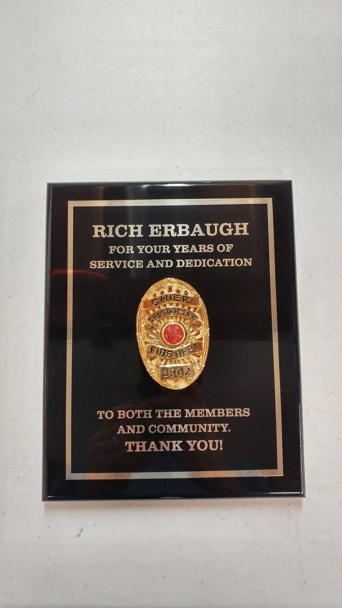 A black commemorative plaque for Rich Erbaugh featuring a centered gold police badge and a message of service and thanks.