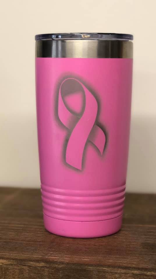 A pink stainless steel tumbler with a grey, laser-engraved breast cancer awareness ribbon in the center.