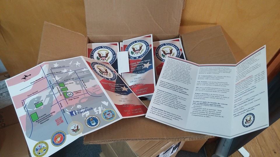 An open cardboard box contains several folded brochures featuring U.S. government seals and patriotic red, white, and blue.