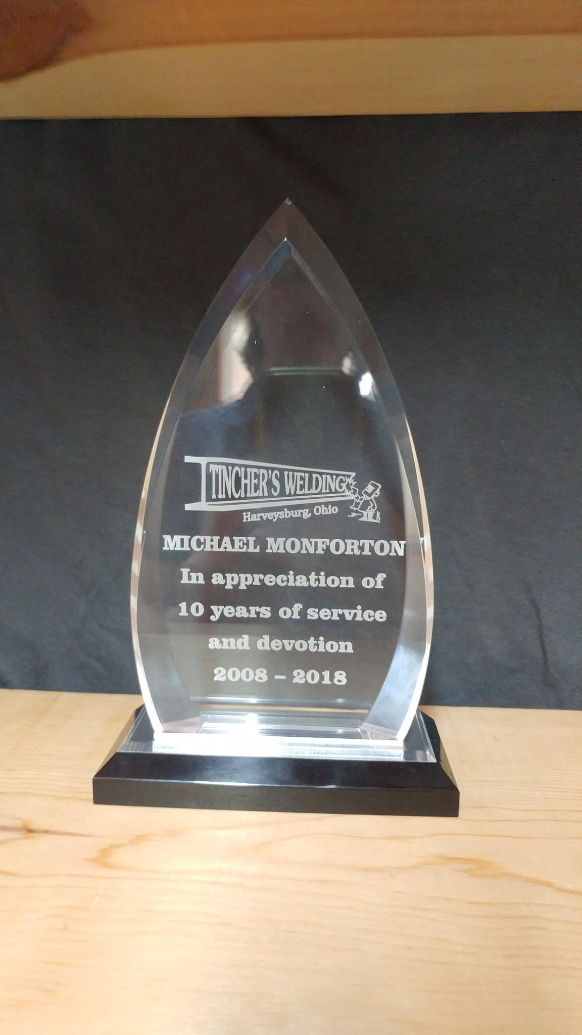 A clear, teardrop-shaped glass award on a black base, engraved with