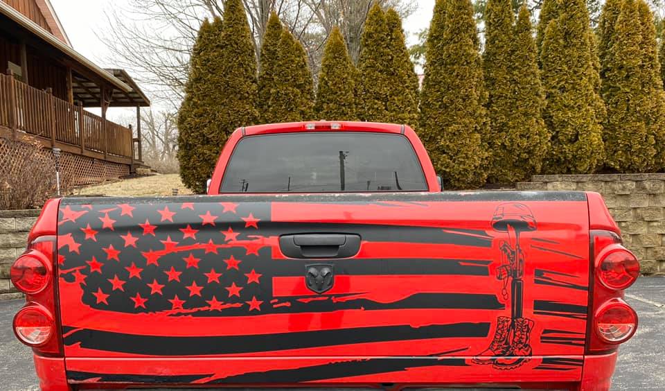 The back of a red pickup truck featuring a black distressed American flag graphic with a pair of boots on the right.