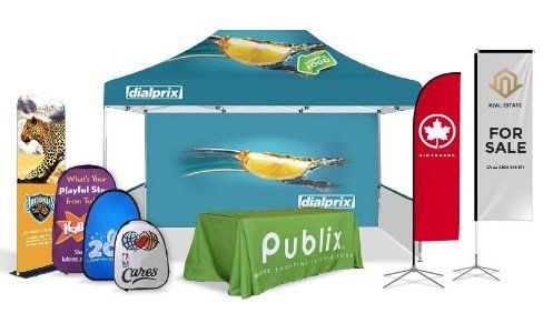A promotional display set featuring a branded tent, a green tablecloth, several banners, and various portable signs.