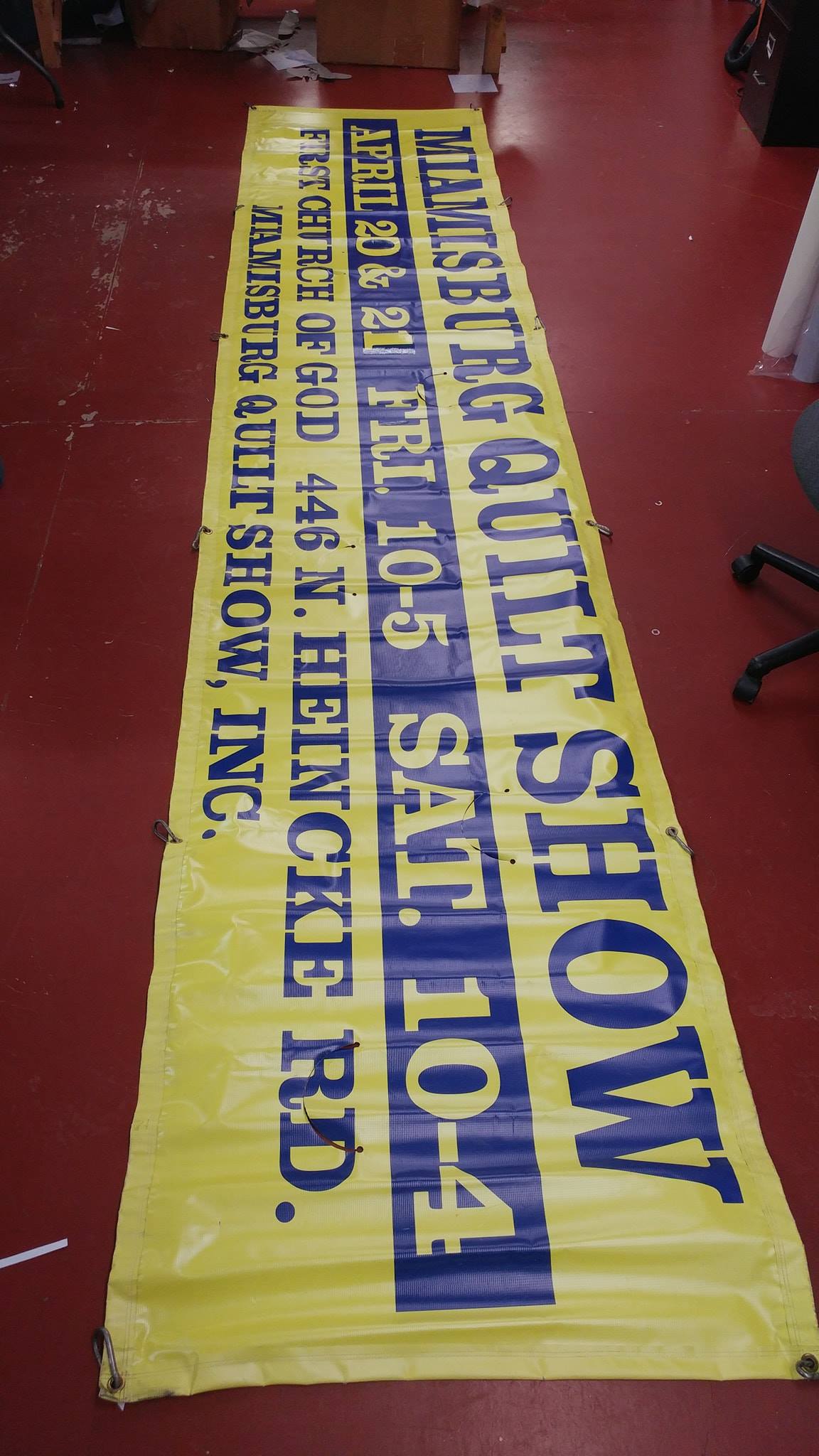 A long yellow banner with blue text announcing the Miamisburg Quilt Show, dates, times, and address.