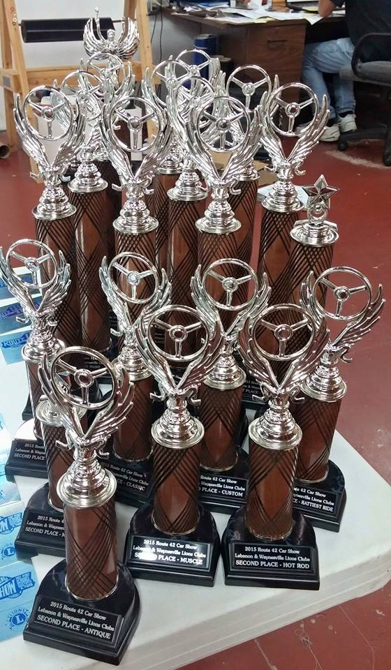 A cluster of silver racing-themed trophies with wood-grain columns and black bases arranged on a white table.
