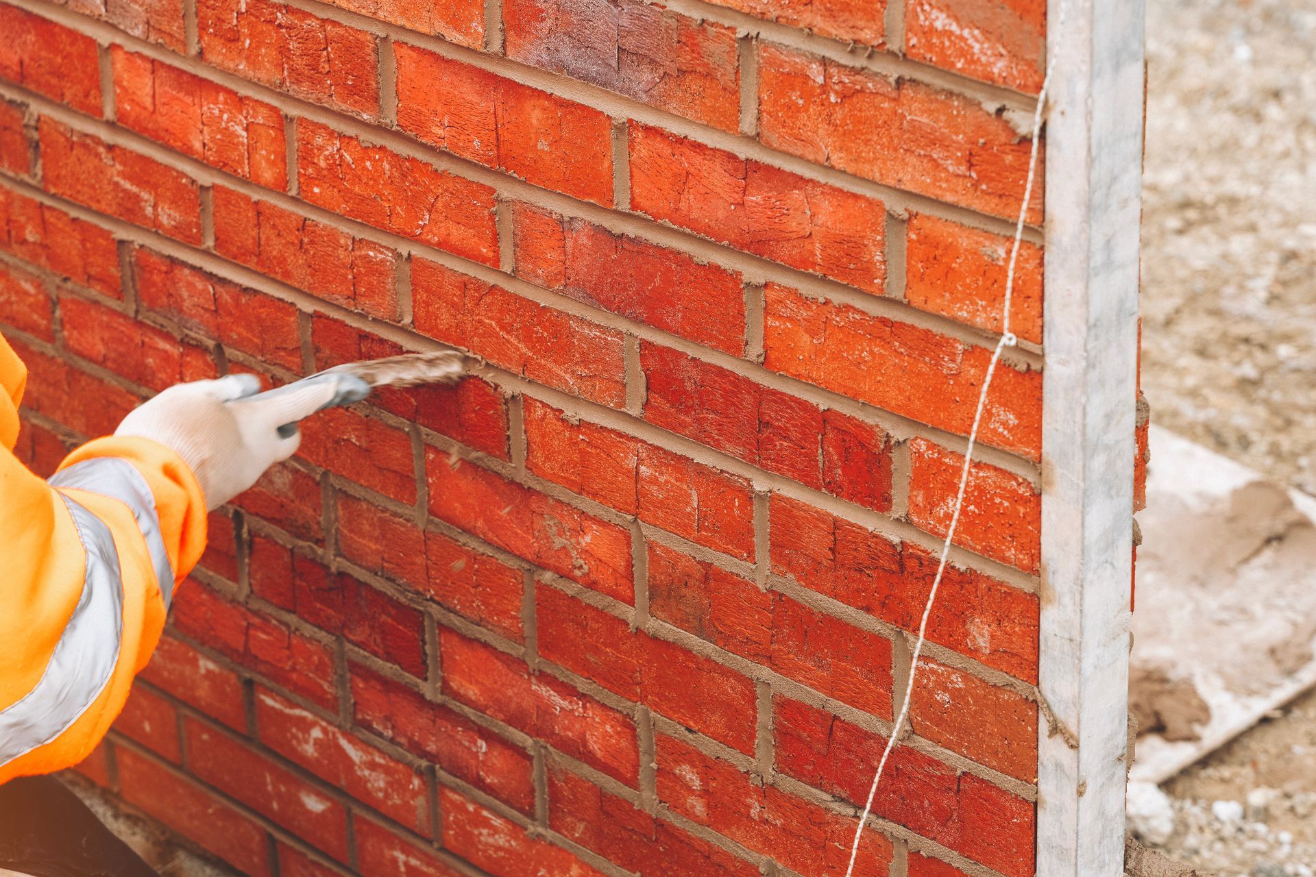 Maçon appliquant du mortier sur un mur de briques rouges, à l'extérieur.