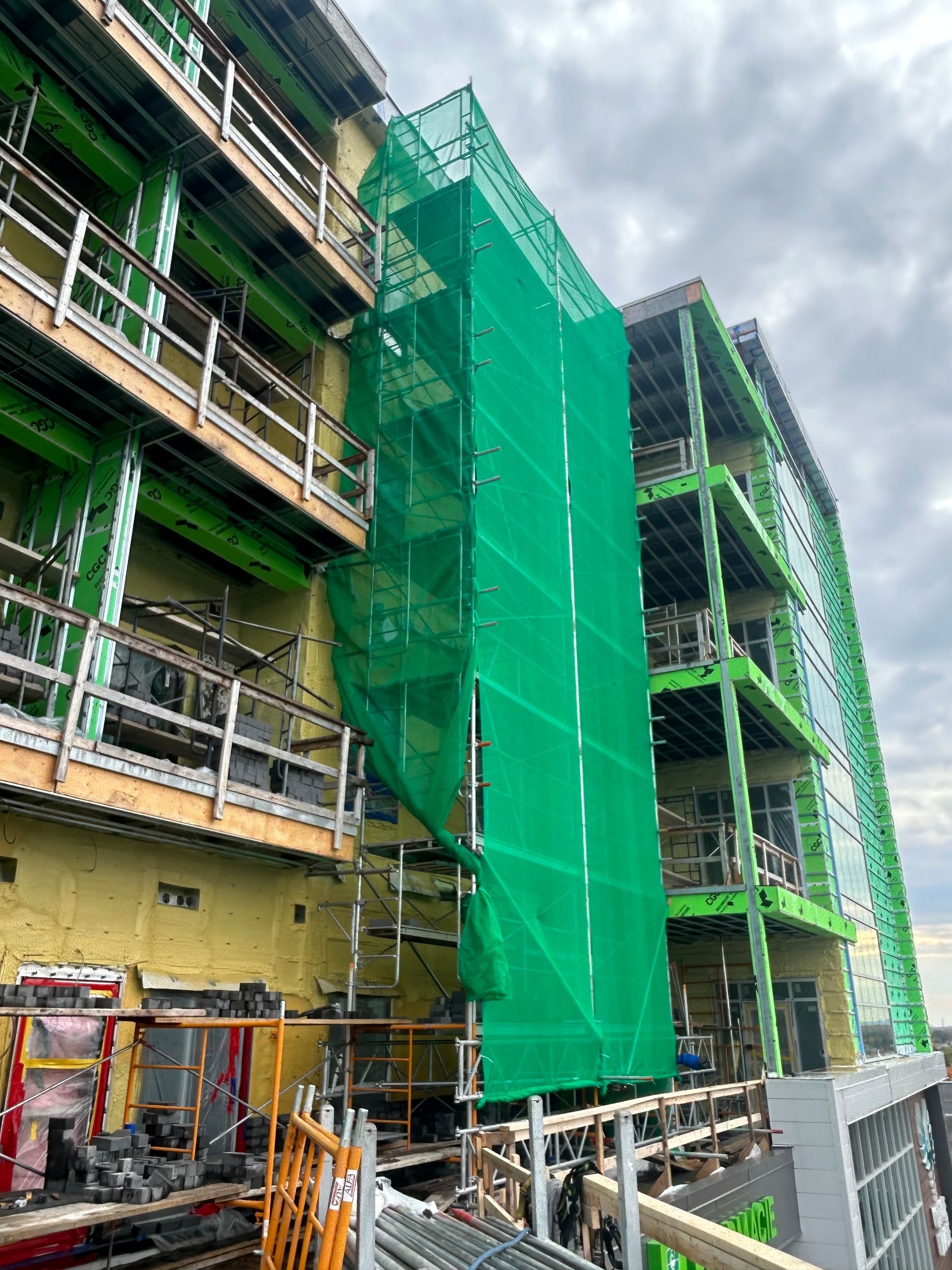 Chantier de construction avec filet vert recouvrant un échafaudage sur un immeuble à plusieurs étages.