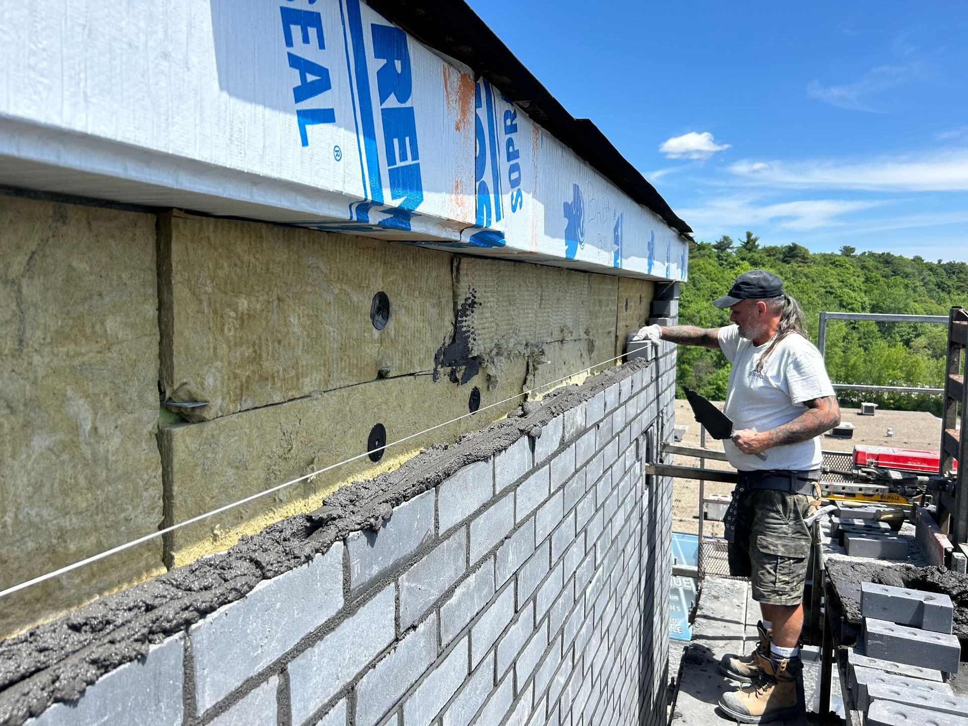 Un homme pose des briques sur la façade d'un bâtiment. Mur isolé, guide-fils et échafaudage. Journée ensoleillée.