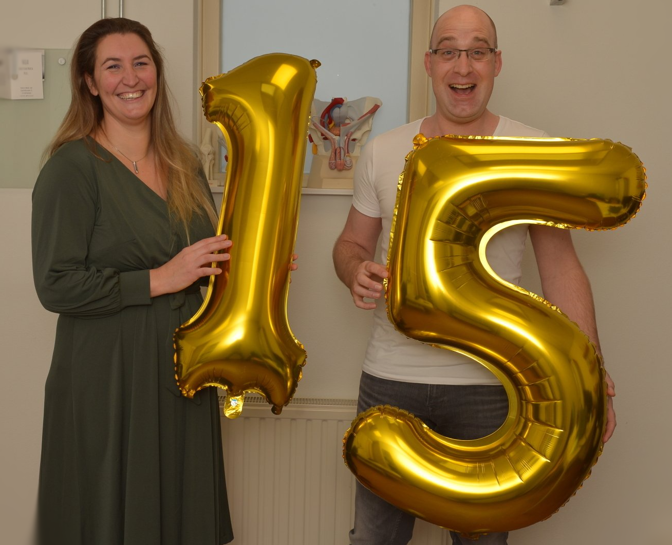 Vrouw en man houden gouden ballonnen vast in de vorm van het getal 15, terwijl ze een jubileum vieren.
