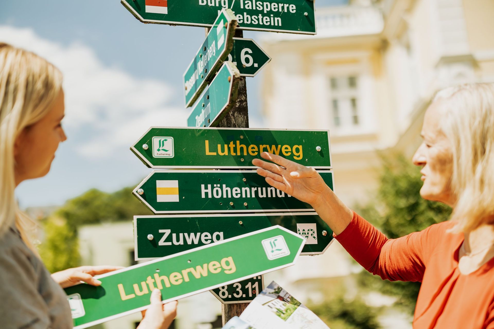 Mitarbeiter des Tourismusverbandes bringen Wanderschilder an einem Pfosten an