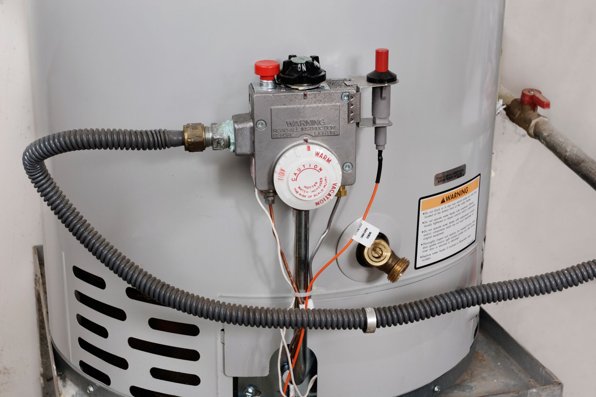 Water heater gas control valve with hoses and wiring attached to a white tank.