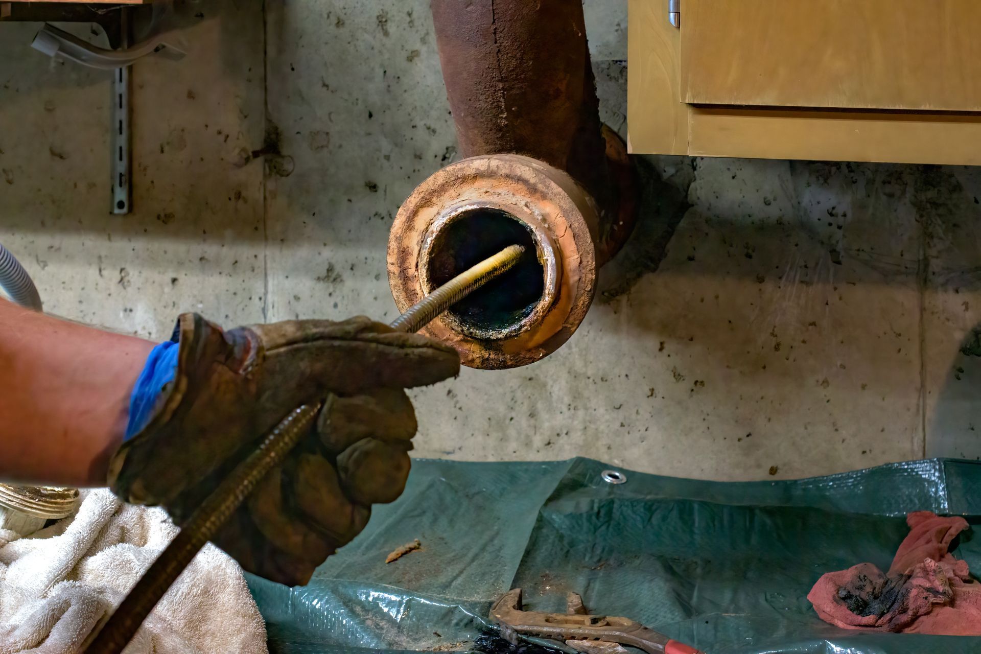 Gloved hand using a pry bar to remove a rusted pipe fitting from a wall opening