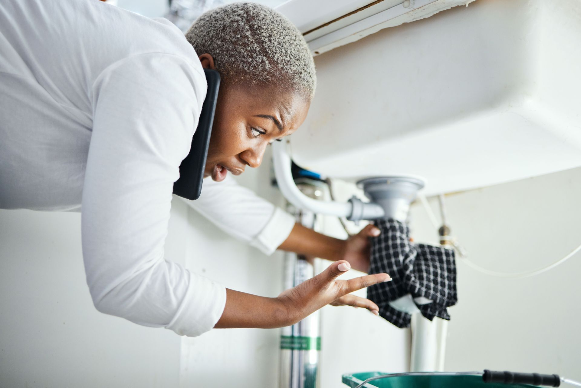 Person adjusting plumbing under a sink with tools in a bright kitchen.