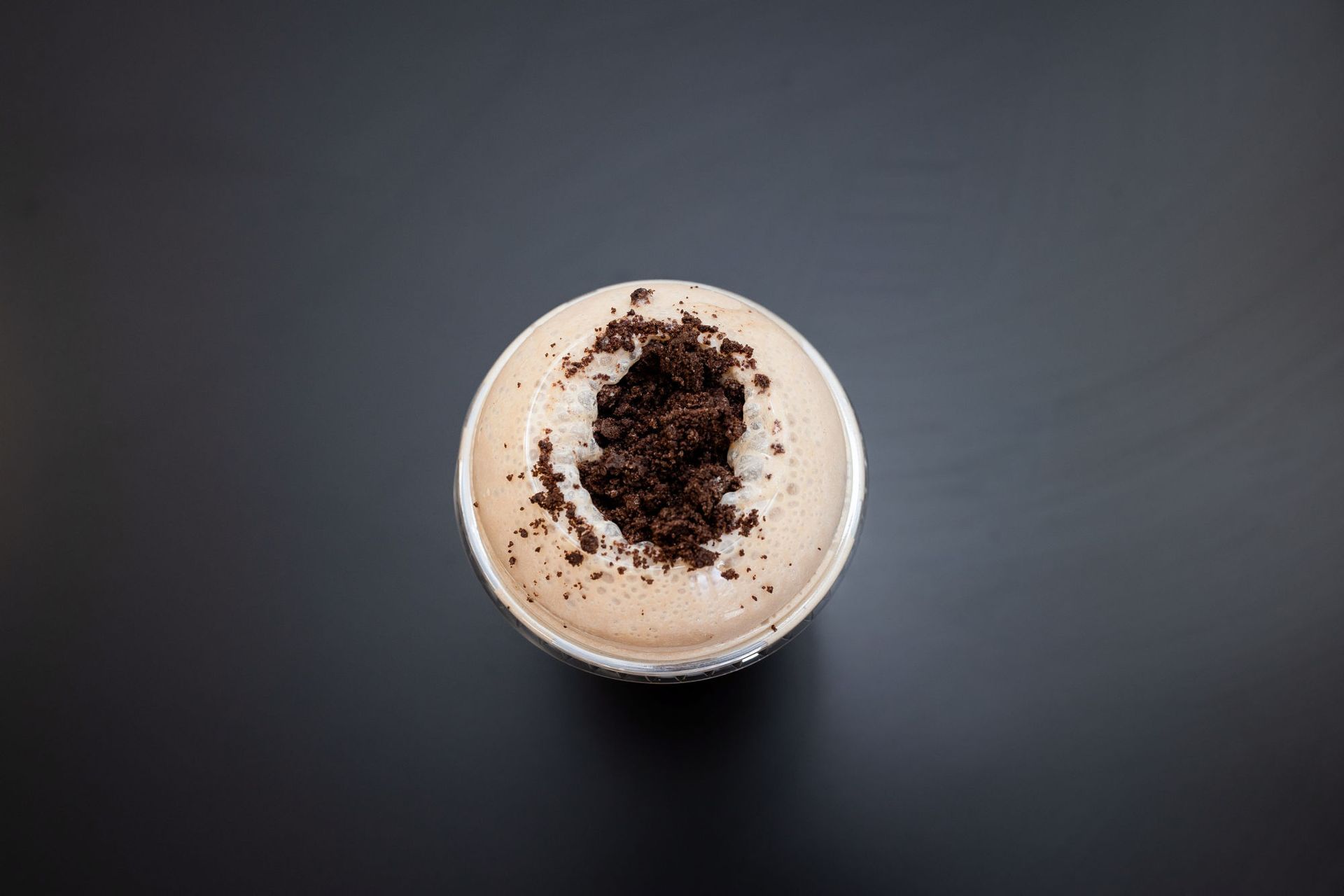 A cup of coffee with oreos on top of it on a black table.