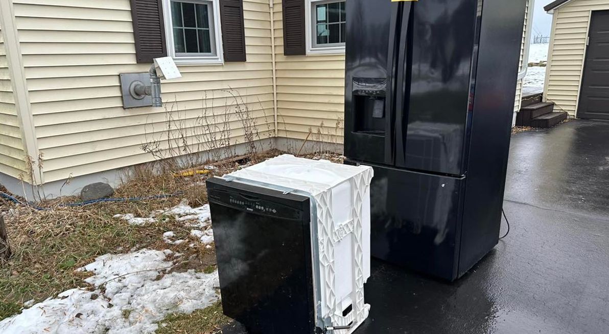 A black refrigerator and a white dishwasher are parked in front of a house.