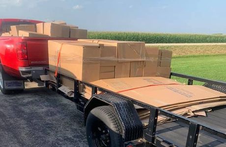A red truck is towing a trailer filled with cardboard boxes.