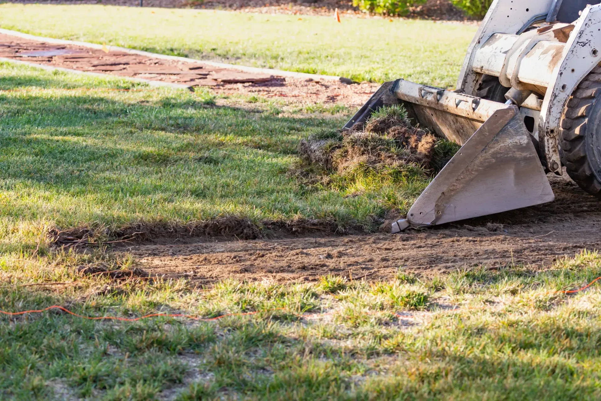 Bulldozer bucket scraping dirt from a grassy field, leaving a dark path