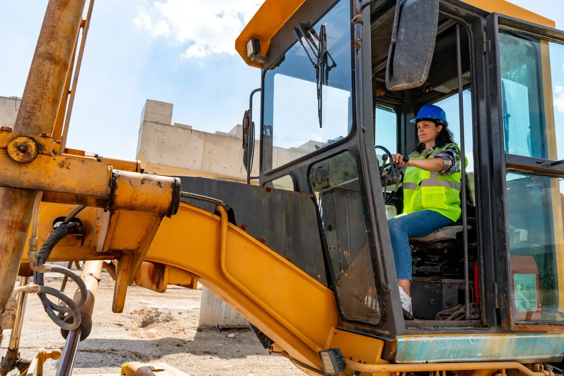 Construction worker in a blue hard hat operating a yellow excavator at a demolition site