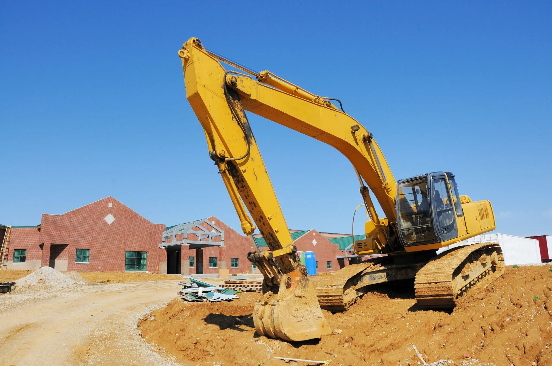 Yellow excavator digging dirt at a construction site near new brick houses.