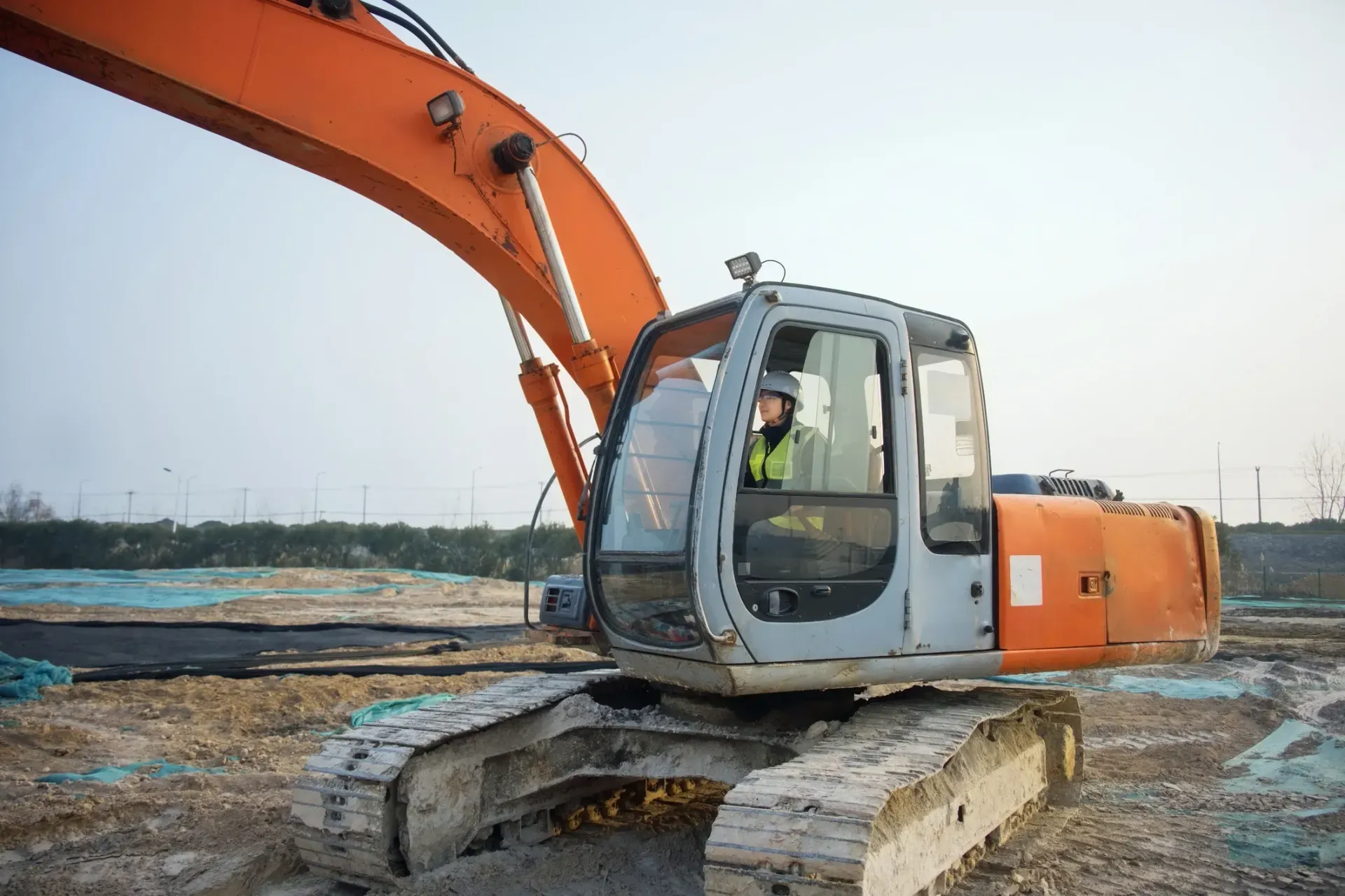 Orange excavator on muddy construction site with operator in cab, arm extended over wet ground