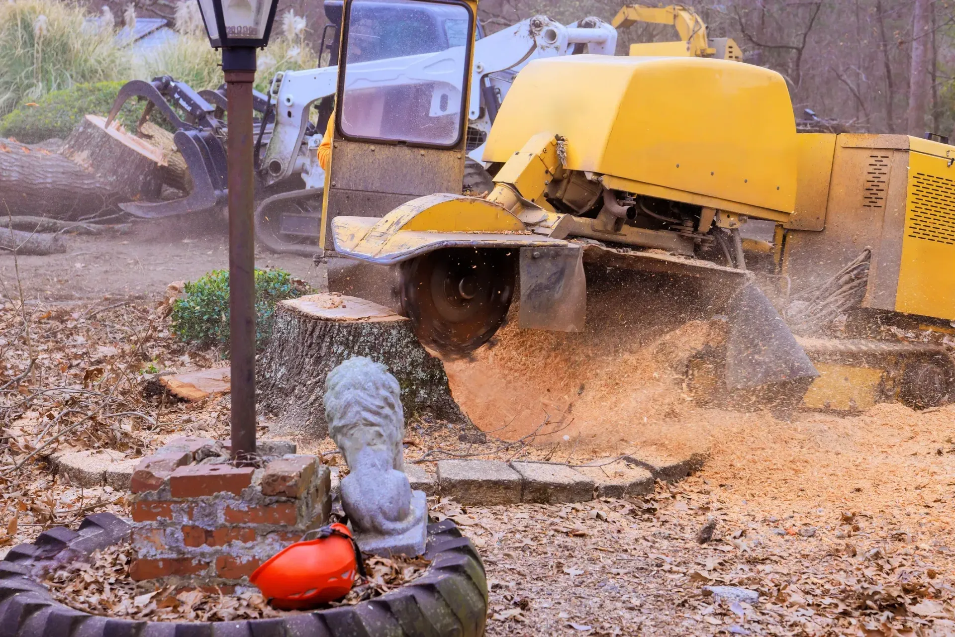 Yellow excavator scooping dirt near a garden bed with a red bucket in the foreground