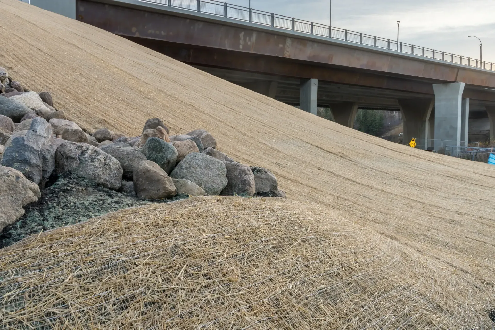 Rock-lined sloped embankment beside a highway overpass under a clear sky