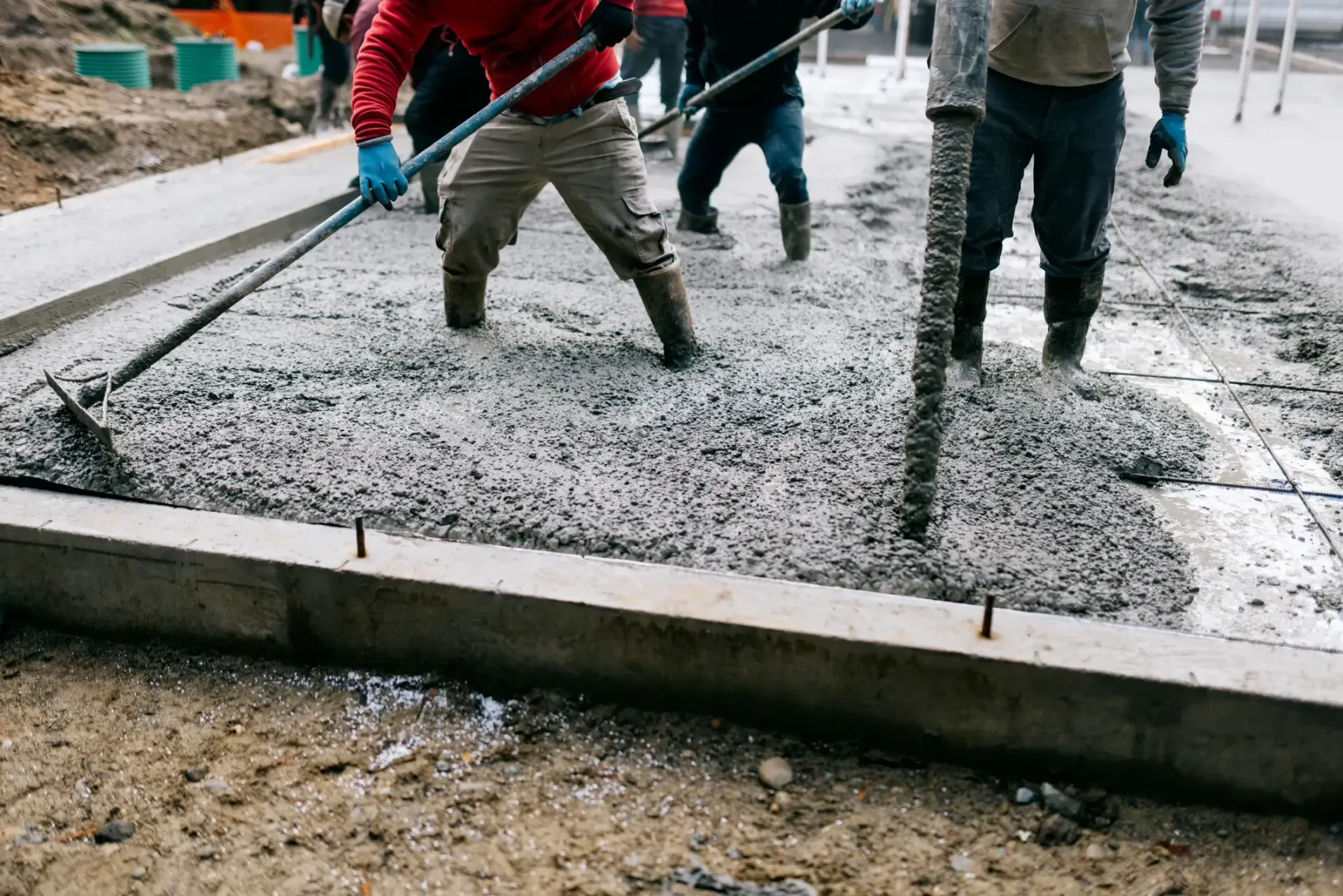 Workers pouring and leveling wet concrete at a construction site with shovels and boots.