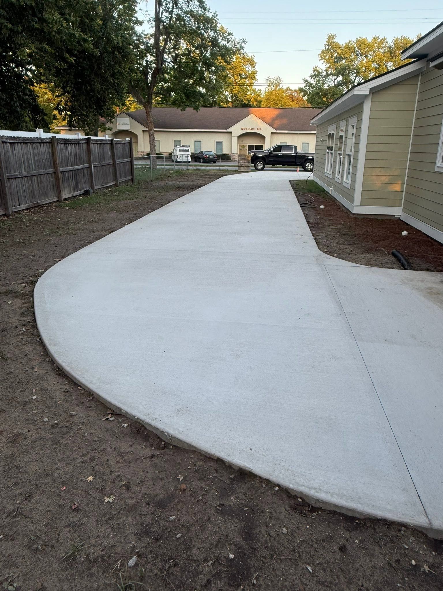 Fresh concrete driveway curving past a house and fence in a backyard area