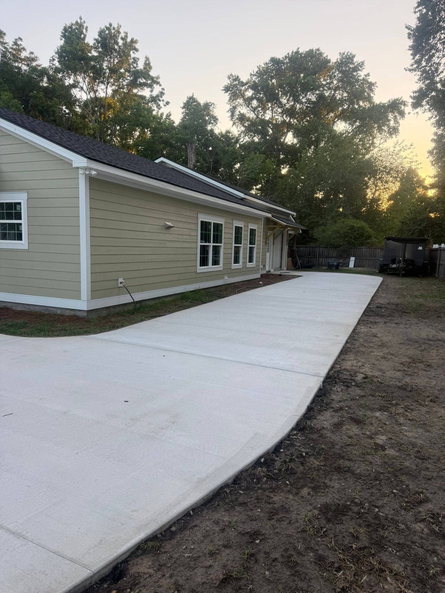 Curved concrete sidewalk beside a tan building at sunset, with trees and dirt around it