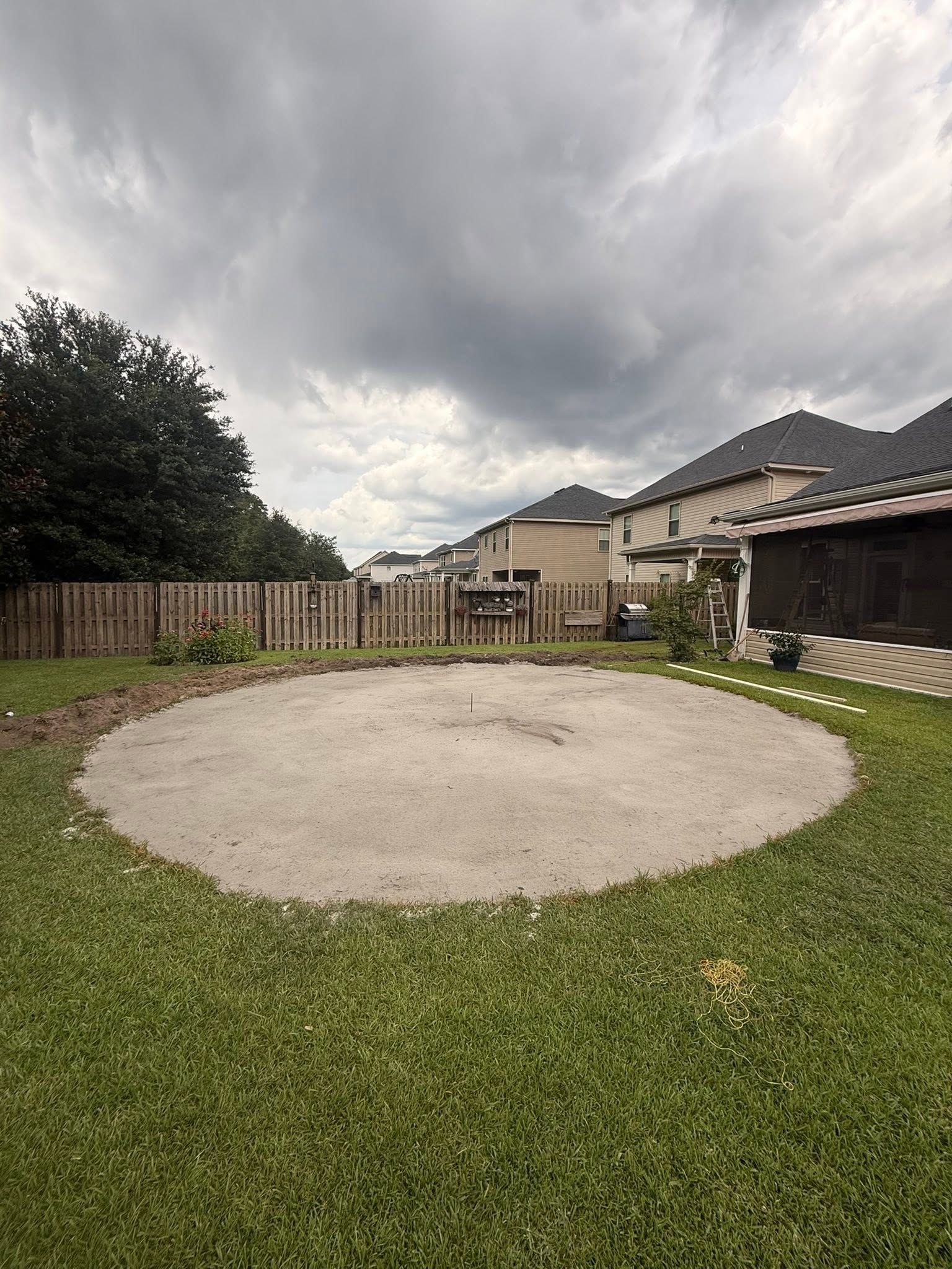 Backyard with a large circular gravel area, green lawn, wooden fence, and cloudy sky