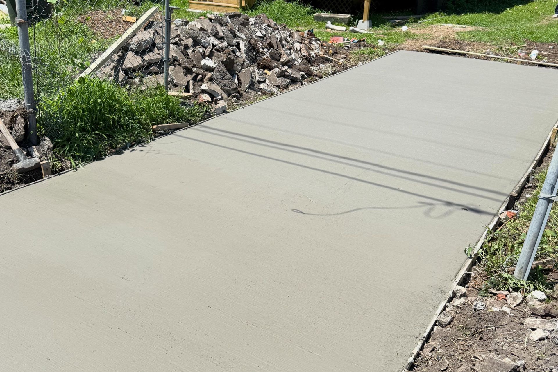 Freshly poured concrete driveway under construction beside rocks and greenery