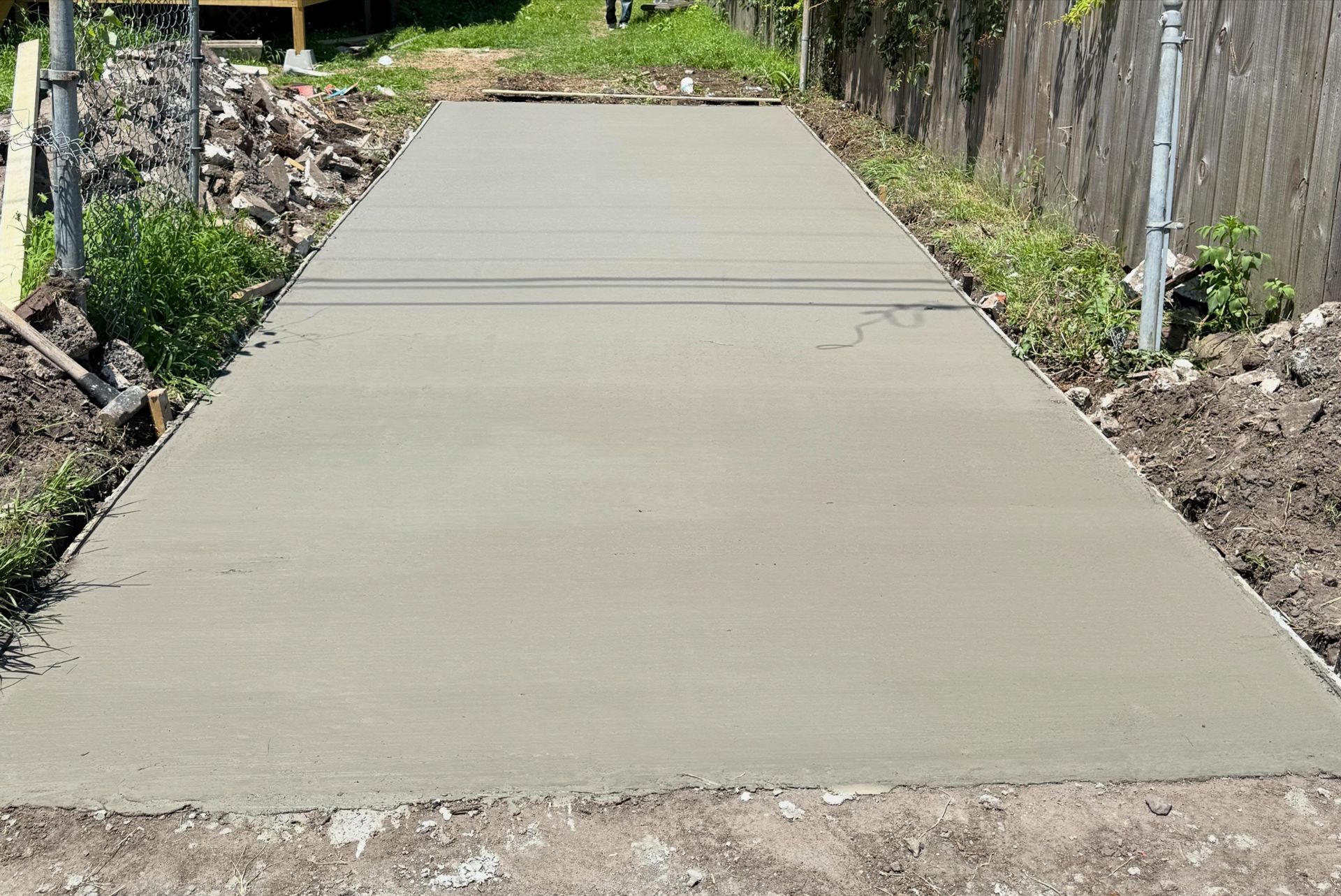 Freshly poured concrete driveway or walkway between dirt and greenery