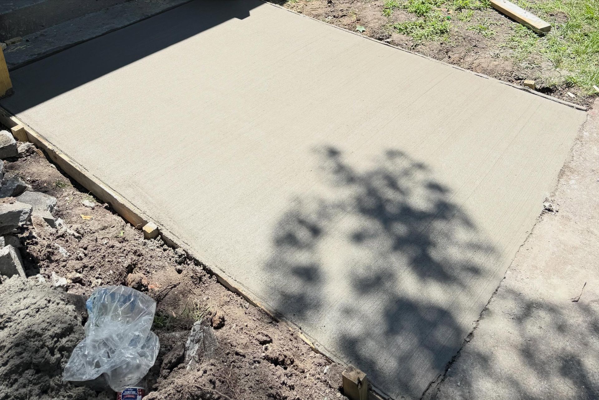 Fresh concrete slab beside a garden bed, with tree shadows on the surface