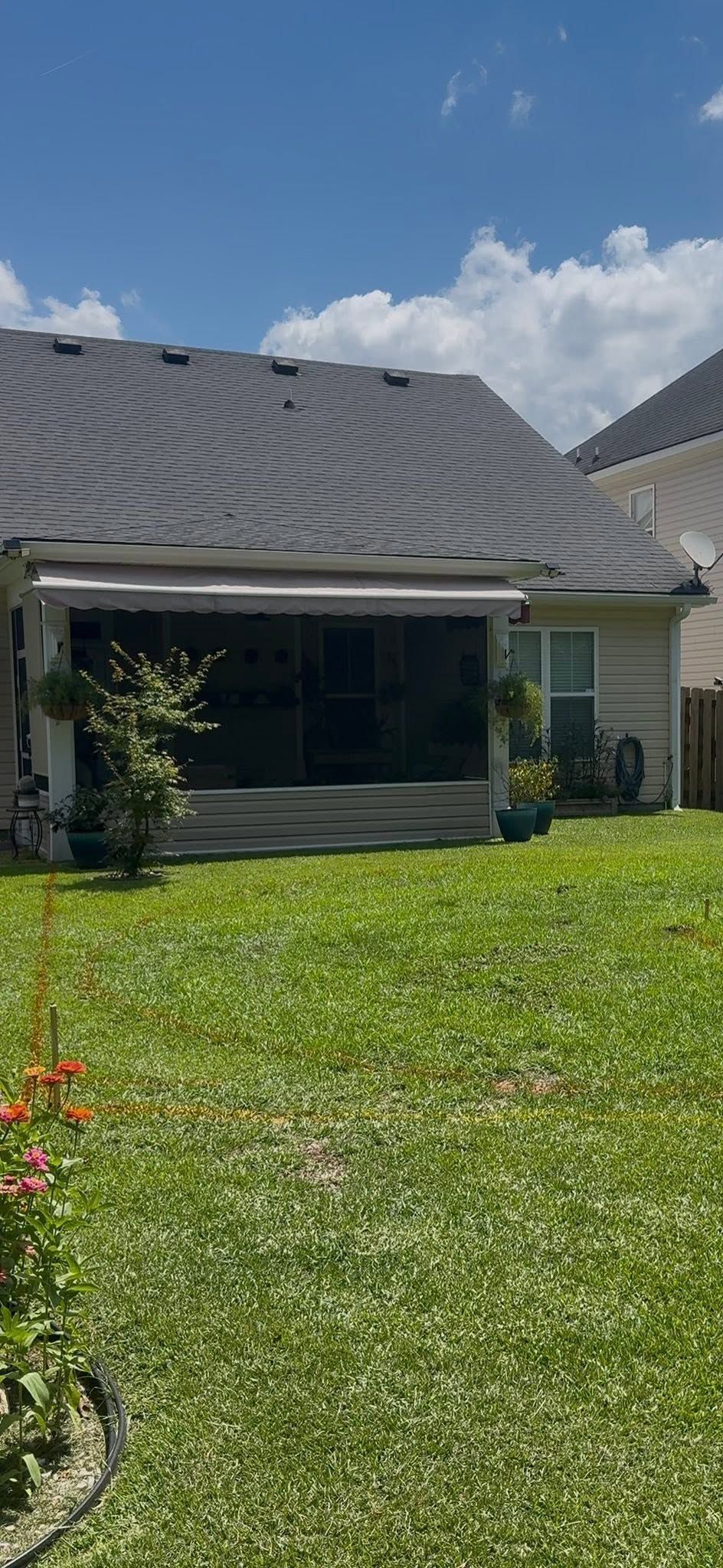 House with dark gray roof and white trim behind a green lawn under a partly cloudy blue sky
