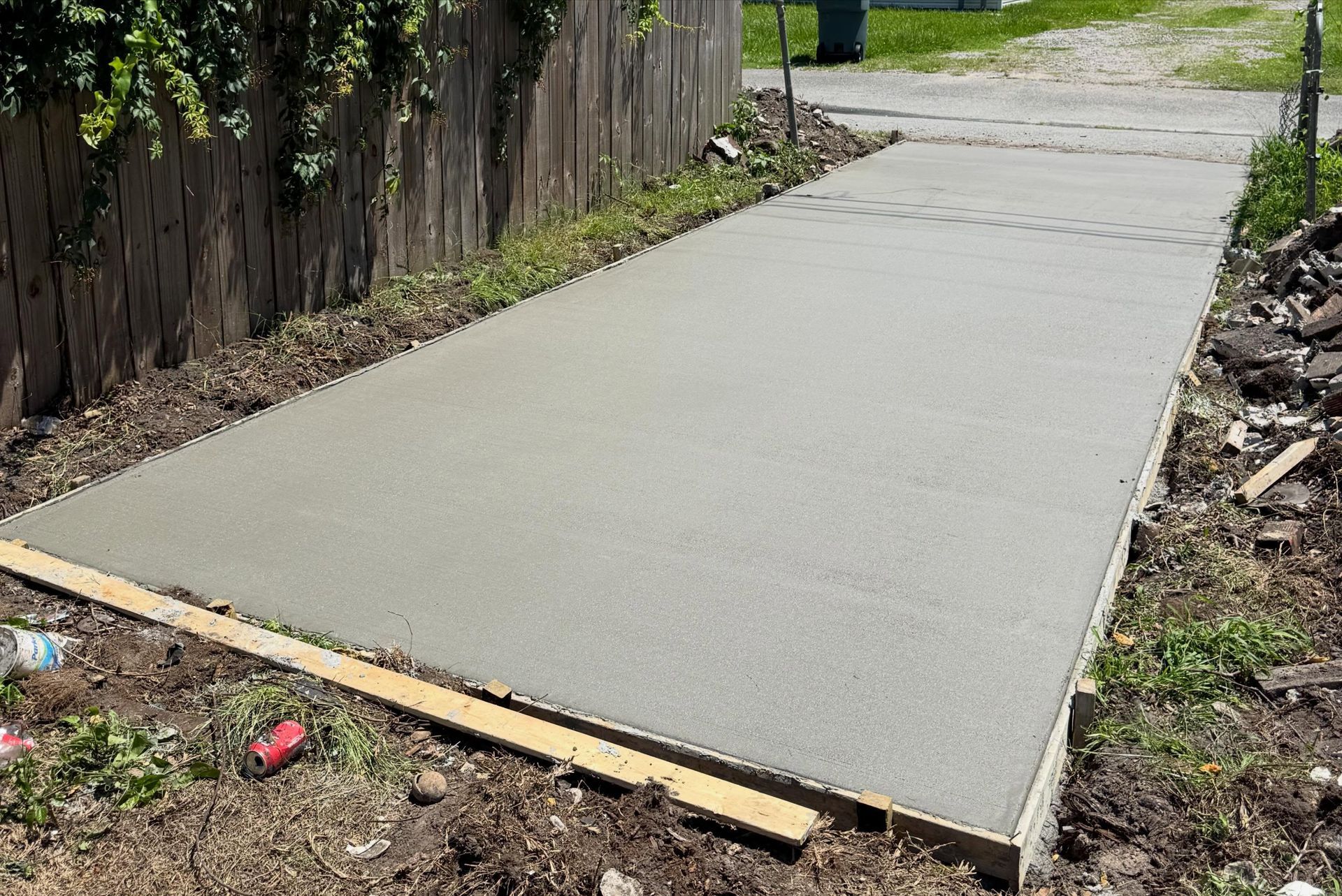 Freshly poured concrete sidewalk beside a wooden fence and dirt edges