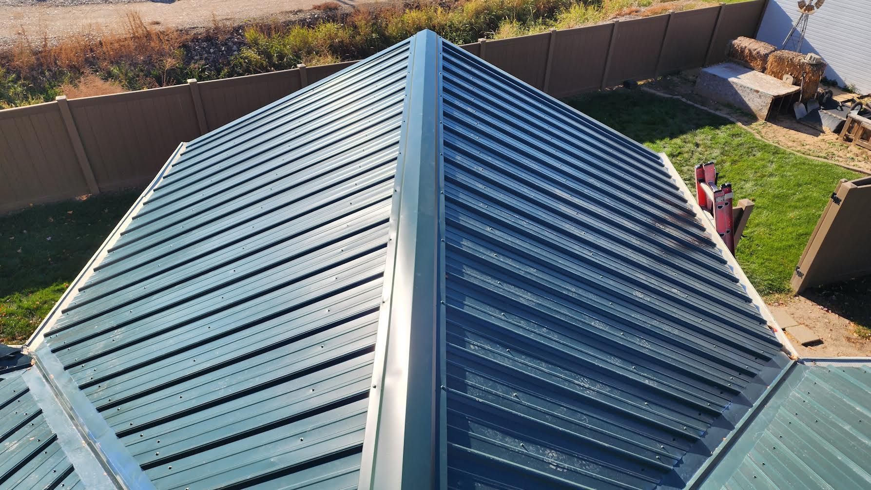 An aerial, high-angle view of a dark green corrugated metal roof with visible ridges and metal ridge capping.
