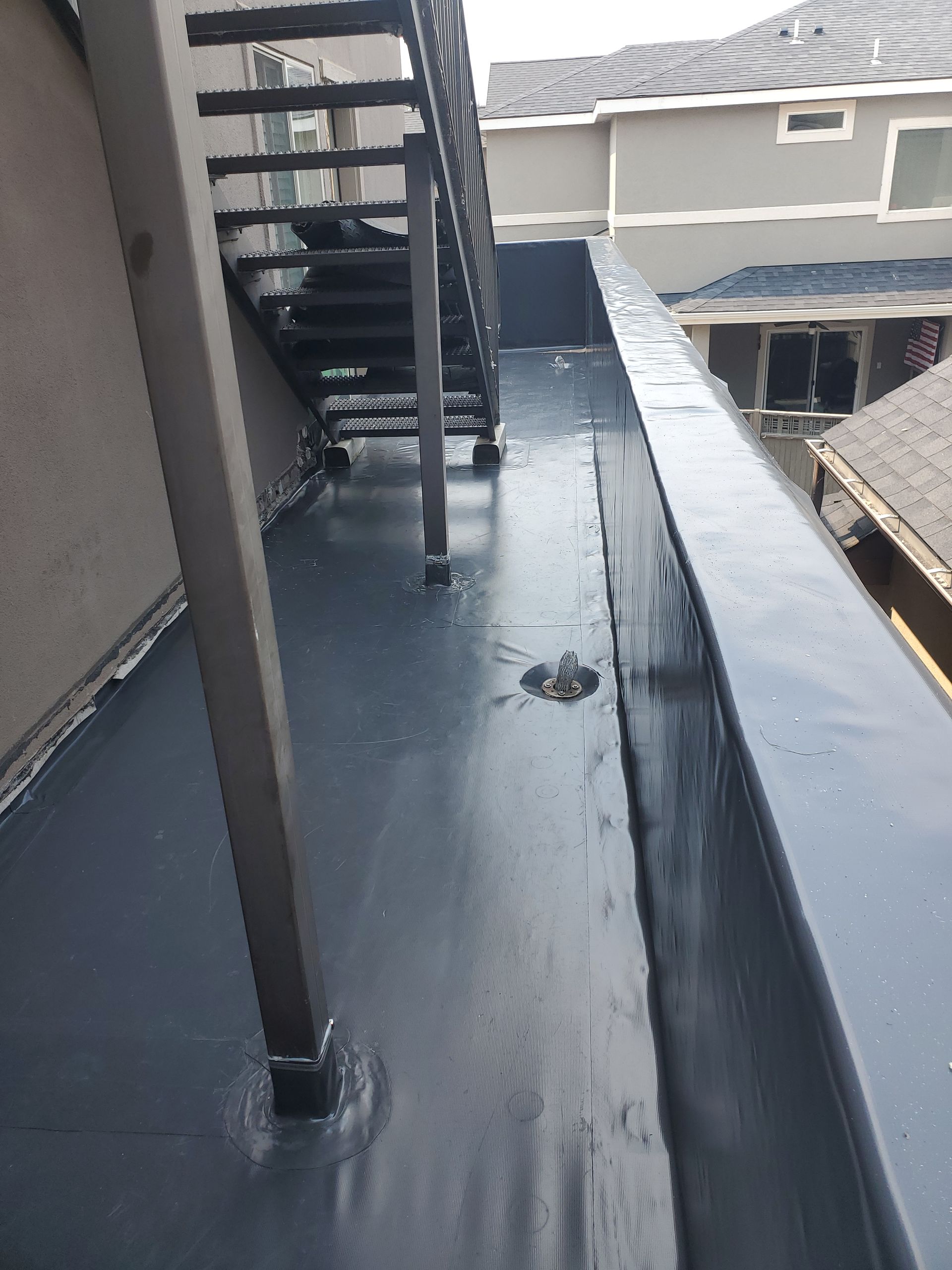 An outdoor metal staircase sits on a balcony with a dark, smooth, waterproof coating on the floor and side wall.