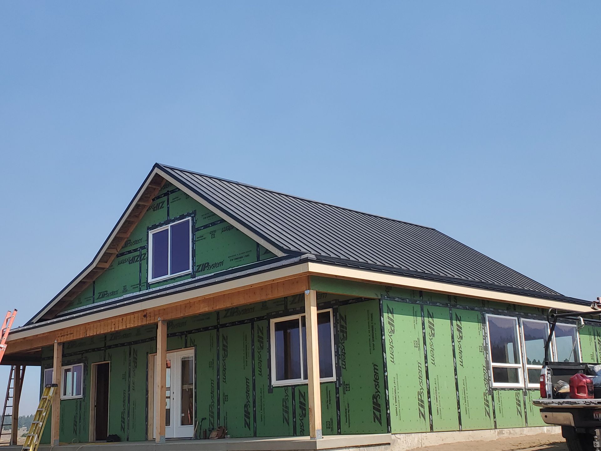 A newly constructed house with a dark roof and green structural sheathing, featuring a front porch and white windows.