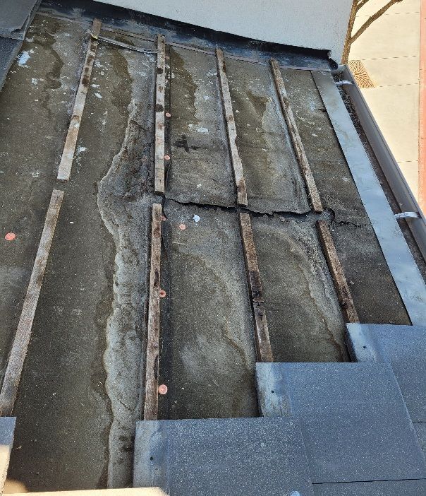 A section of a residential roof under repair, showing dark underlayment, vertical wooden battens, and partially laid tiles.
