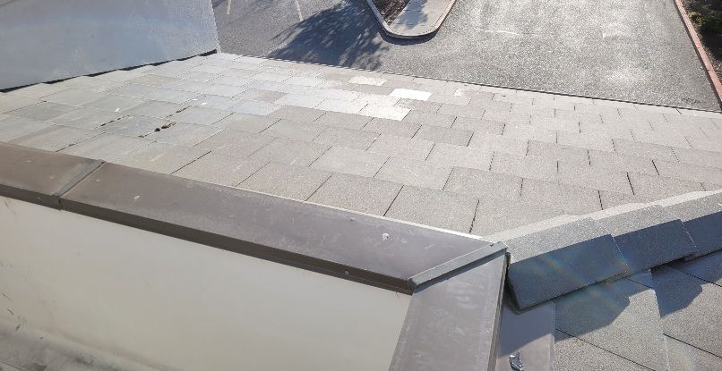 A high-angle view of a tiled residential roof with a skylight and a gray shingled surface.