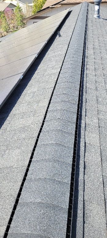 A view of a shingled roof with a ridge vent running along the top peak, adjacent to a section of solar panels.