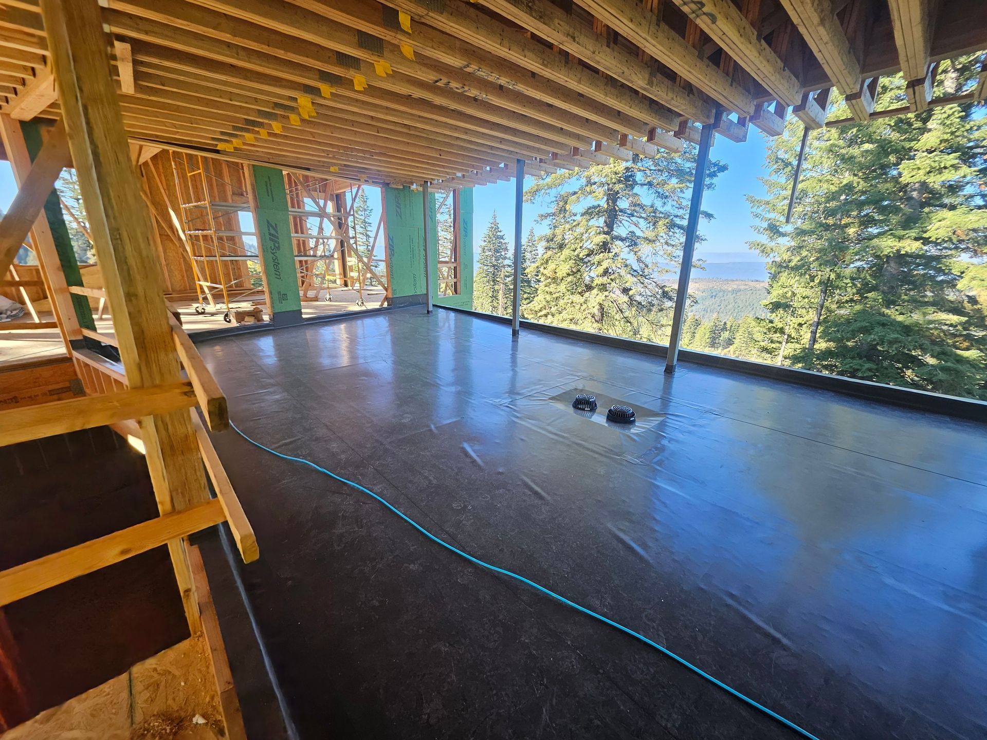 A wooden home under construction with a dark subfloor, open frame walls, and a scenic mountain view in the background.