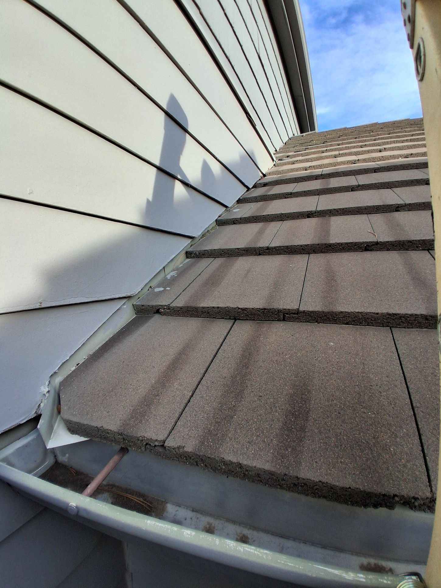 A roof junction where brown concrete tiles meet white horizontal siding, showing a metal gutter below.