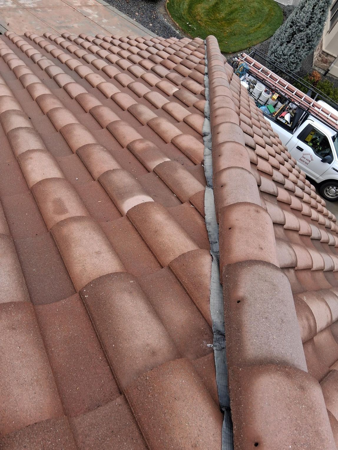 A high-angle view of a brown concrete tile roof with a central ridge line sealed with gray mortar.