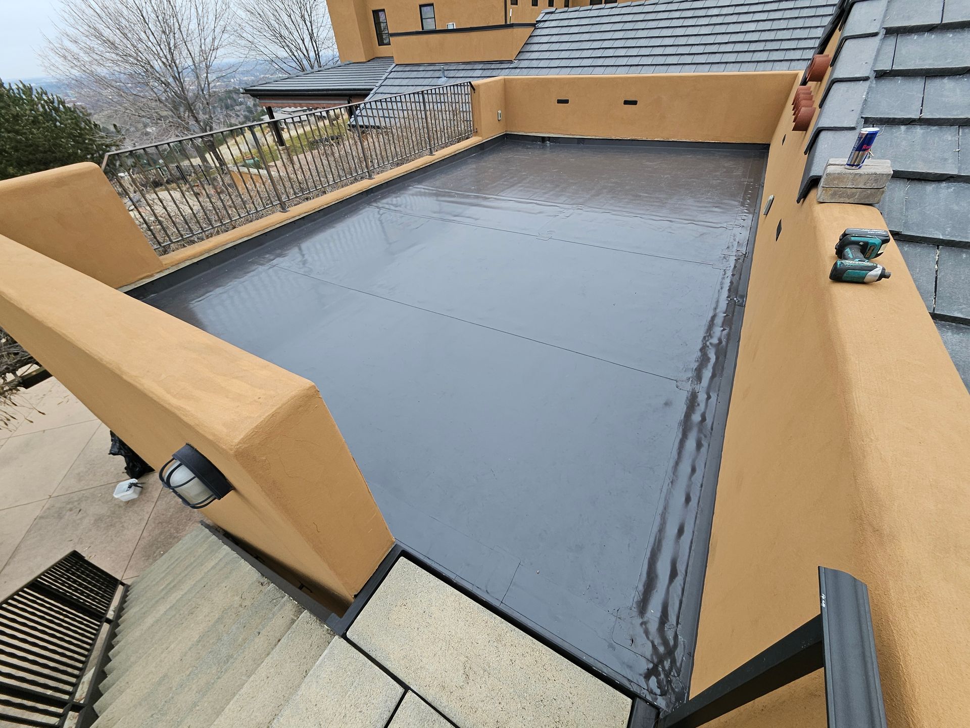 A high-angle view of a newly installed, smooth grey rubber roof enclosed by beige stucco walls on a residential home.