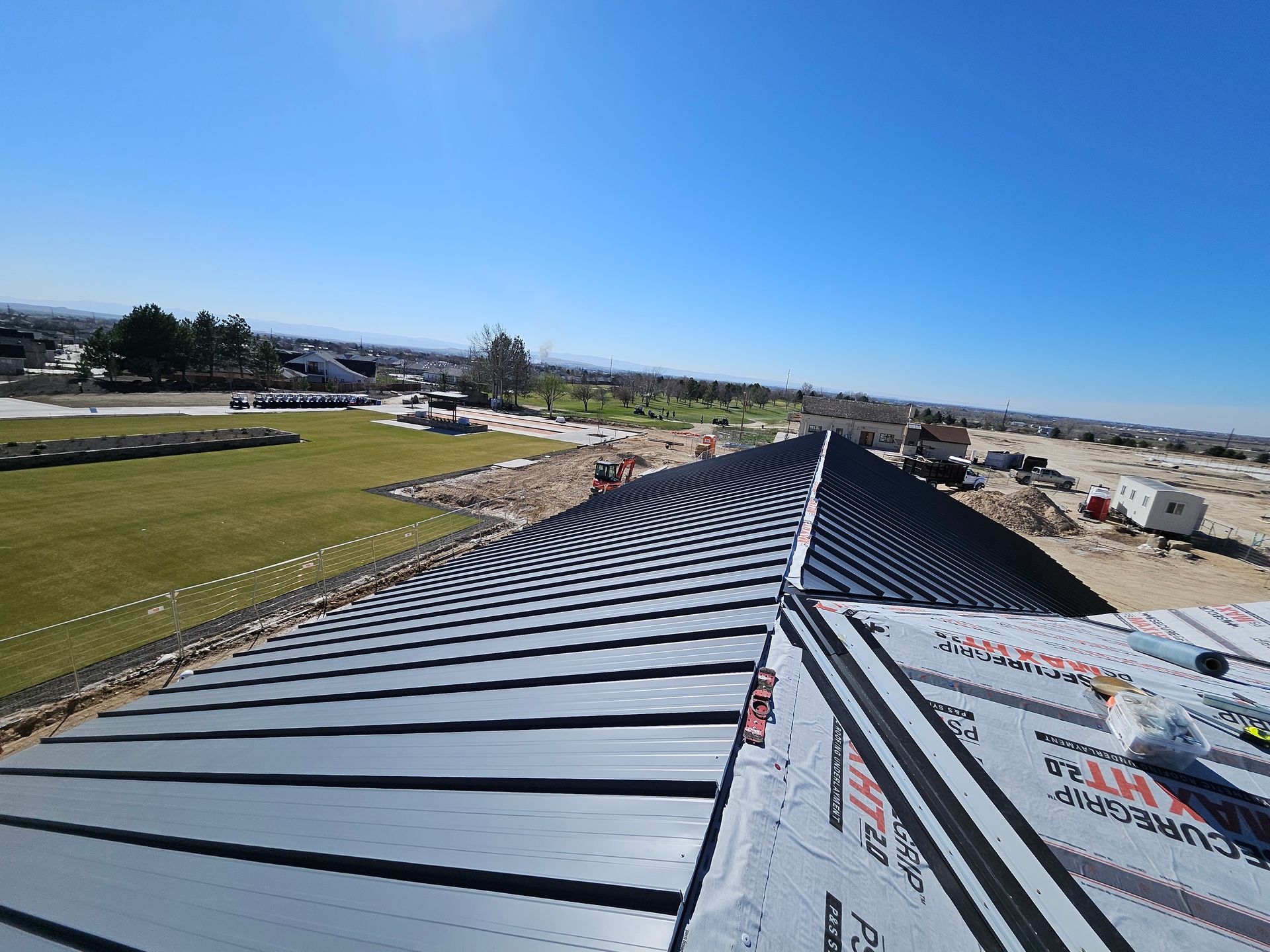 A metal roof under construction, featuring dark ribbed panels beside sections of grey roofing underlayment.