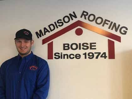 Man in blue shirt and cap stands in front of a Madison Roofing sign, Boise, since 1974.
