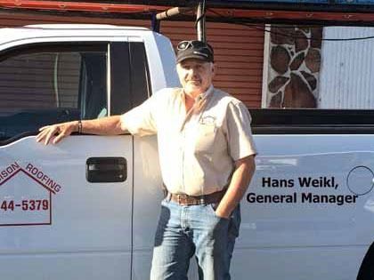 Man in a light shirt and jeans stands next to a white truck with
