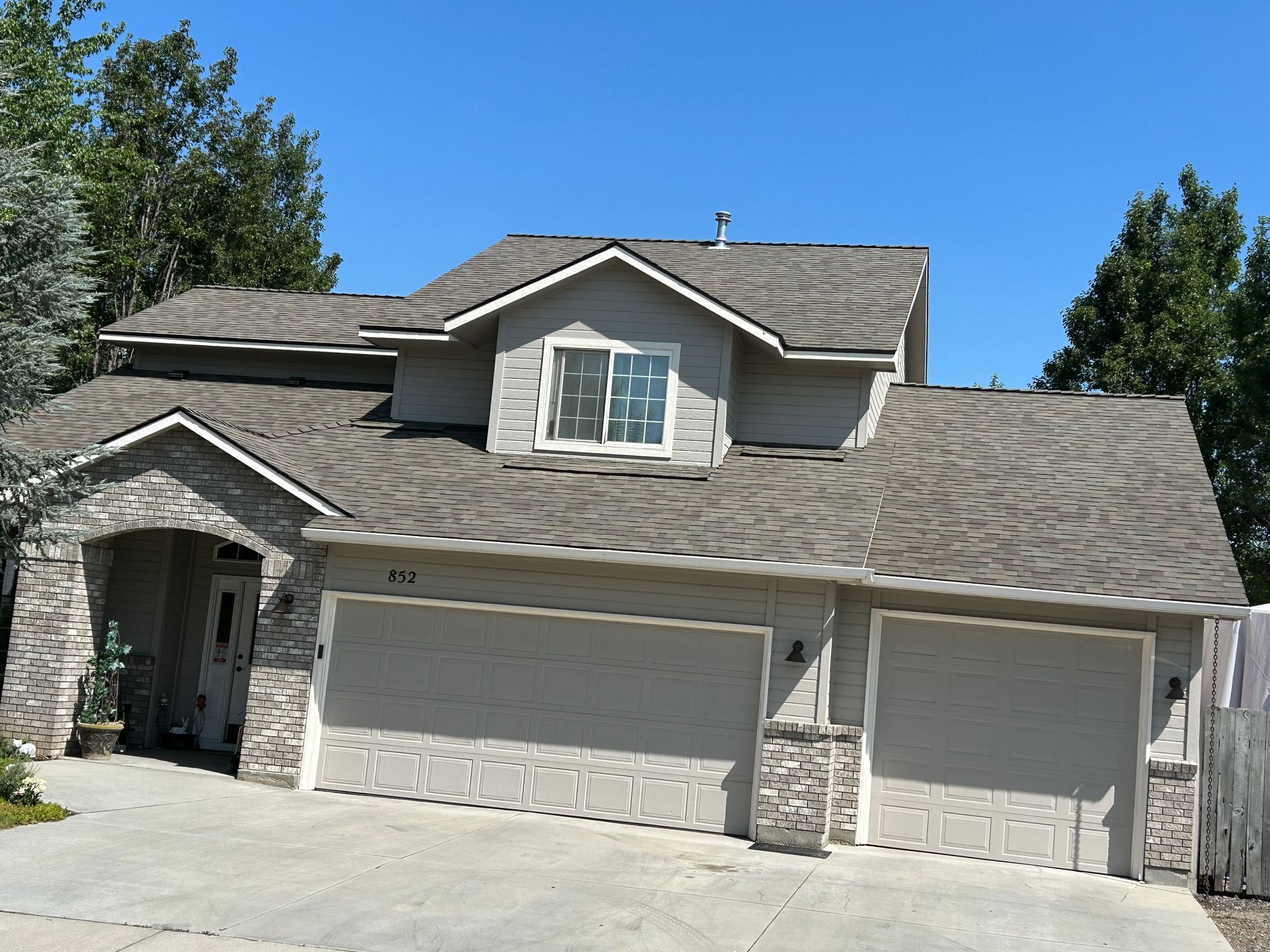 A two-story suburban home with a stone and tan siding exterior, a two-car garage, and a concrete driveway.